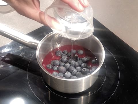 Ajout du sirop de glucose sur les myrtilles et la purée de cassis, dans la casserole posée sur la plaque de cuisson