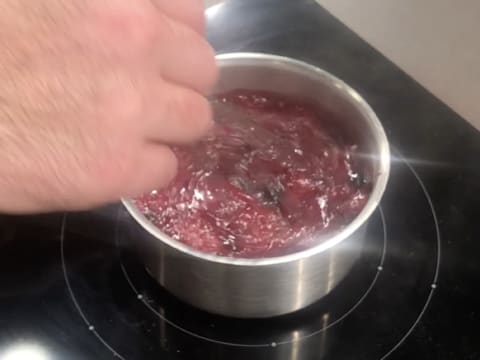 La préparation au cassis est en train de bouillir dans la casserole, tout en étant mélangée au fouet