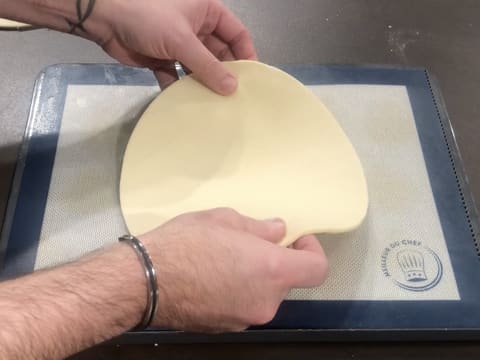 Un disque de pâte feuilletée inversée est déposé sur une plaque à pâtisserie recouverte d'un tapis de cuisson en silicone