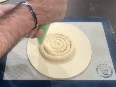 La crème frangipane est pochée en forme de spirale sur le disque de pâte feuilletée inversée qui se trouve sur une plaque à pâtisserie recouverte d'un tapis de cuisson en silicone