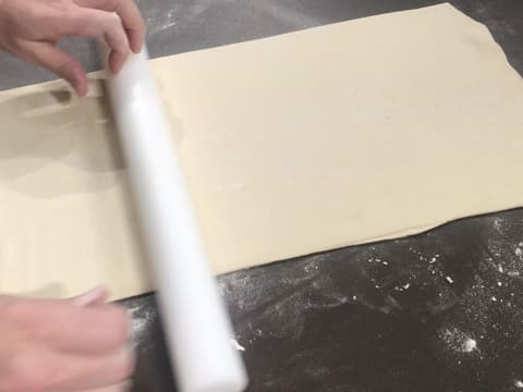 La pâte feuilletée est abaissée en un grand rectangle avec le rouleau à pâtisserie, sur le plan de travail légèrement fariné