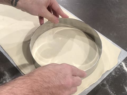 Un grand cercle à mousse est placé sur l'abaisse de pâte feuilletée qui est sur une feuille de papier sulfurisé