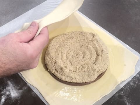 La partie gauche du grand rectangle de pâte feuilletée est soulevée pour recouvrir le disque de gianduja recouvert de crème frangipane noisette