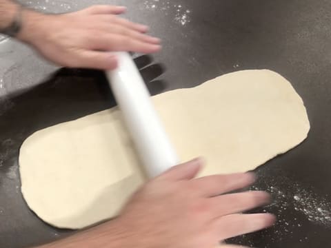 La pâte est abaissée en une bande au rouleau à pâtisserie sur le plan de travail fleuré