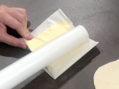 Le beurre de tourage qui est enveloppé dans une feuille de papier sulfurisé est tapé et aplati avec le rouleau à pâtisserie