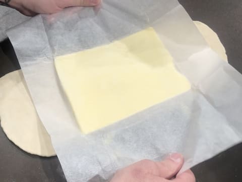 Le beurre de tourage qui est abaissé en un rectangle est posé au milieu de la pâte étalée en une bande, et la feuille de papier sulfurisé est enlevée