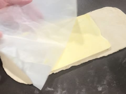 Le beurre de tourage qui est abaissé en un rectangle est posé au milieu de la pâte étalée en une bande, et la feuille de papier sulfurisé est enlevée