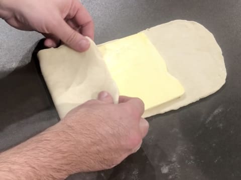 La partie inférieure de la pâte est rabattue sur la première moitié du beurre de tourage