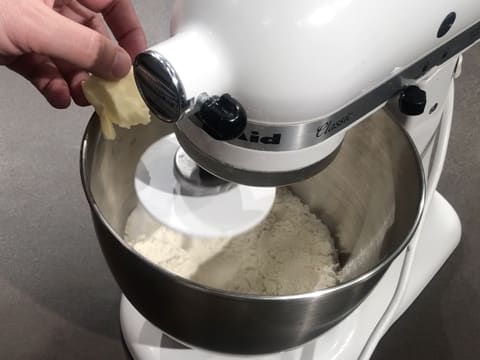 Ajout du beurre pommade sur la farine dans la cuve du batteur qui est muni de l'accessoire crochet