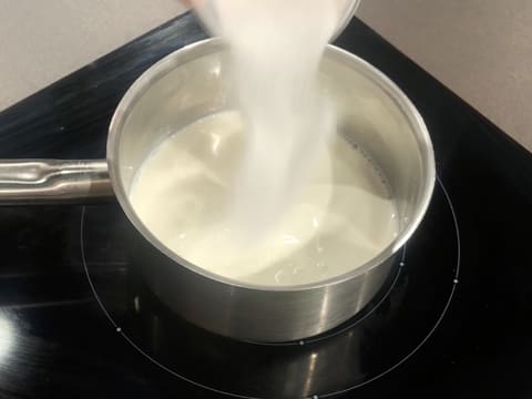 Du sucre en poudre est versé sur le lait dans la casserole qui est posée sur la plaque de cuisson