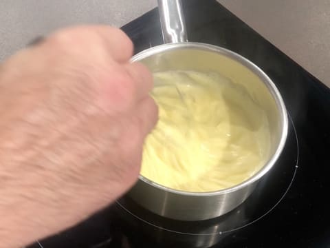 La crème est en train de cuire dans la casserole, tout en étant mélangée au fouet