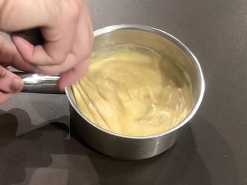 Incorporation de la pâte de noisette dans la crème pâtissière à l'aide du fouet, dans la casserole posée sur le plan de travail