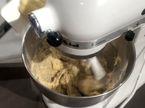Ajout de la crème pâtissière noisette sur la préparation qui est en train d'être mélangée dans la cuve du batteur, avec l'accessoire feuille