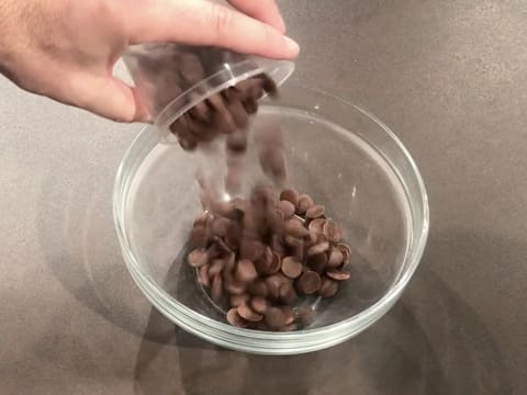 Les pistoles de chocolat au lait sont versées dans un saladier en verre qui est posé sur le plan de travail