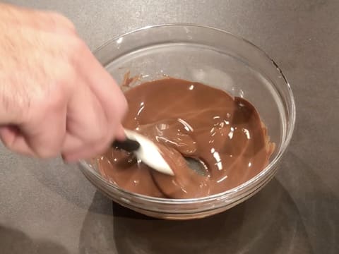 Le chocolat au lait fondu est mélangé à l'aide d'une spatule type maryse, dans le saladier posé sur le plan de travail