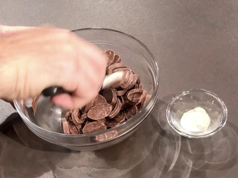 Les ingrédients pour la couronne en chocolat sont un bol de chocolat au lait à gauche de la photo et un petit récipient contenant du beurre de cacao Mycryo sur la droite