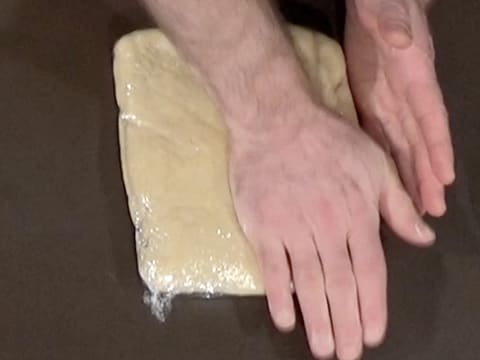 La pâte emballée dans le film alimentaire est aplatie avec la paume de la main