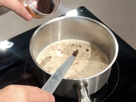 Ajout d'une pointe de couteau de vanille en poudre dans la casserole contenant le lait