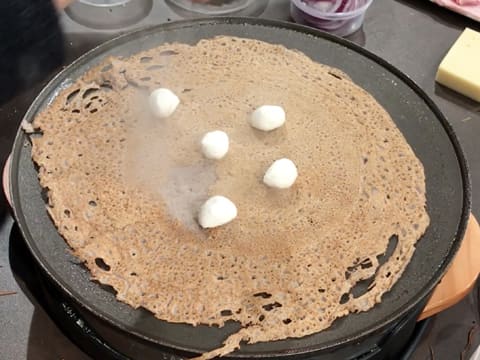 Des boulettes de mozzarella sont déposées sur la galette qui est en train de cuire sur la crêpière électrique