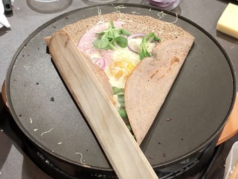 Un second côté de la galette est plié à l'aide de la spatule en bois, de façon à former un triangle