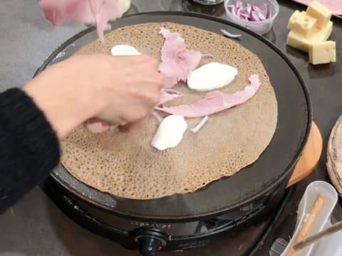 Ajout de morceaux de jambon blanc et de mozzarella sur la galette qui cuit sur la crêpière électrique