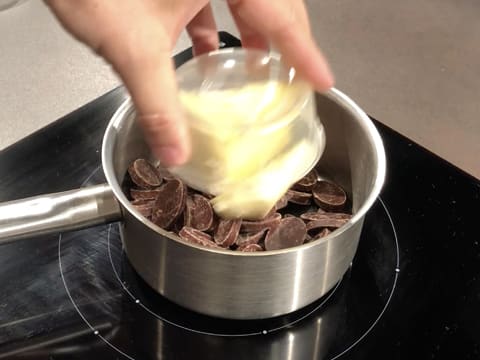 Le beurre est versé sur les fèves de chocolat noir qui se trouvent dans la casserole posée sur la plaque de cuisson