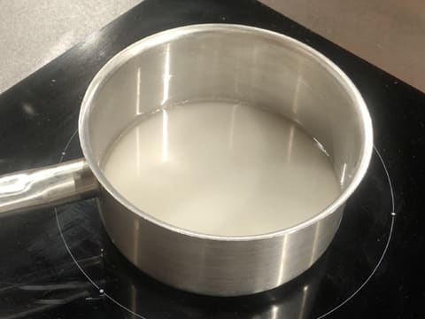 L'eau et le sucre en poudre sont en train de chauffer dans la casserole posée sur la plaque de cuisson