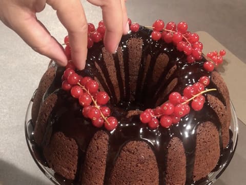 Des groseilles égrappées sont placées à la surface de l'entremets, sur le glaçage au chocolat