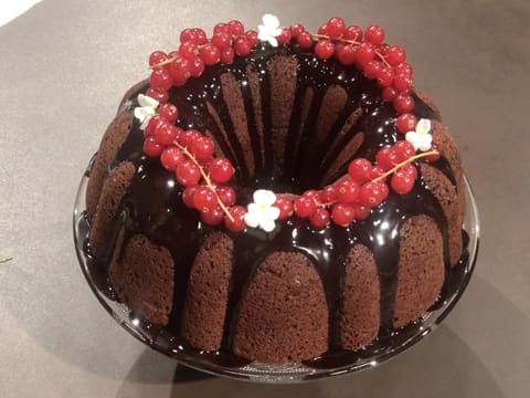 Obtention du gâteau au chocolat noir facile décoré du glaçage au chocolat, des groseilles fraîches et des pensées blanches, présenté sur une assiette de service