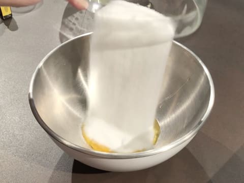 Du sucre en poudre est versé sur les jaunes d'œufs dans un cul de poule placé sur le plan de travail
