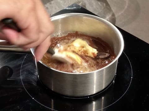 Mélange à la spatule maryse du beurre et des fèves de chocolat noir qui sont partiellement fondus dans la casserole posée sur la plaque de cuisson