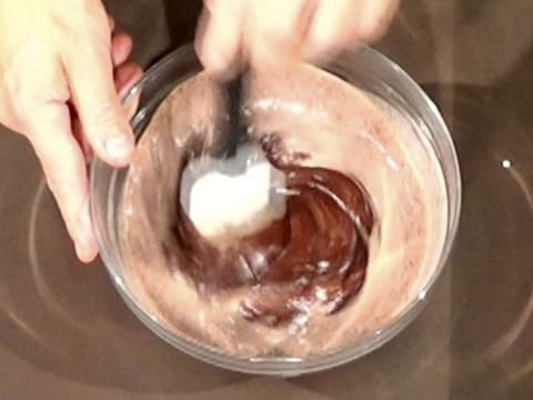 La crème liquide et le chocolat noir fondu sont mélangés dans le saladier à l'aide de la spatule maryse