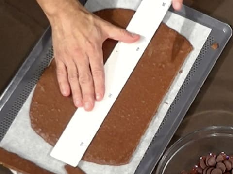 Mesure du croustillant chocolat qui est sur une plaque à pâtisserie perforée recouverte d'une feuille de papier sulfurisé, avec une règle graduée