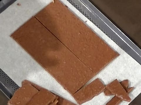 Obtention de deux rectangles de croustillant chocolat sur une plaque à pâtisserie perforée recouverte d'une feuille de papier sulfurisé