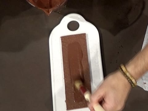 Un peu de glaçage chocolat est étalé sur la semelle en croustillant chocolat avec un pinceau pâtissier