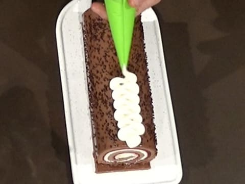 La Chantilly vanille est pochée en zig zag à la poche à douille sur le gâteau forêt noire qui est posé sur le plat de service