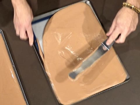 La pâte à choux au chocolat est étalée sur la deuxième plaque à pâtisserie recouverte d'un tapis de cuisson en silicone