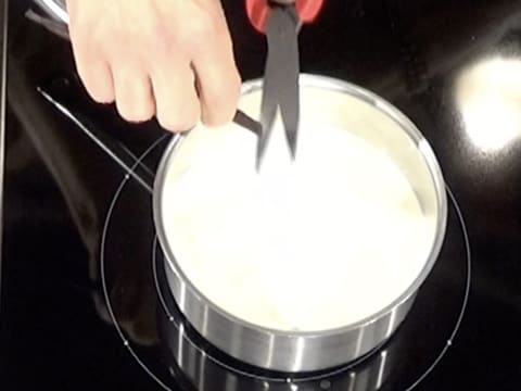 Le bâton de vanille est coupé en morceaux avec une paire de ciseaux, au-dessus de la casserole contenant la crème liquide