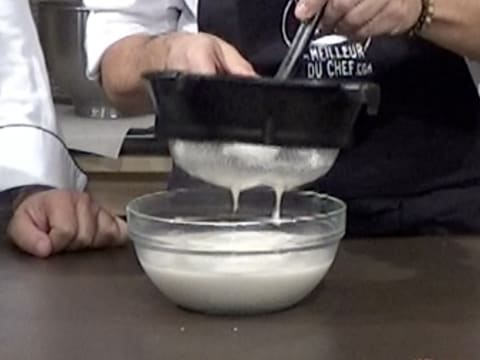 La crème est filtrée dans la passoire tamis, au-dessus du saladier, tout en écrasant une spatule type maryse dans la passoire pour faire passer toute la crème et les grains de vanille