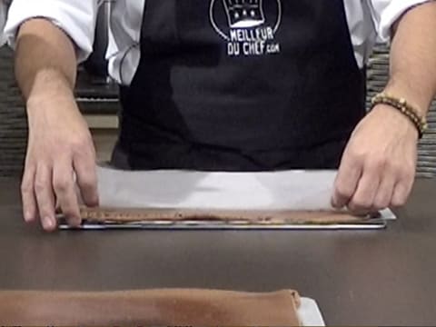 Une feuille de papier sulfurisé est déposée sur le biscuit au chocolat qui est sur une plaque à pâtisserie, sur le plan de travail