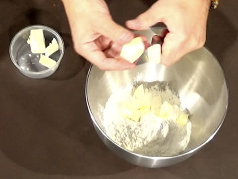 Le beurre est coupé en morceaux au-dessus de la cuve du batteur qui contient les poudres