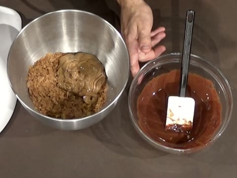 La cuve du batteur contenant le crumble, le pailleté feuilletine et le praliné noisette est sur le plan de travail à gauche, et à droite se trouve le saladier dans lequel il y a le mélange de chocolat noir et de beurre de cacao fondus