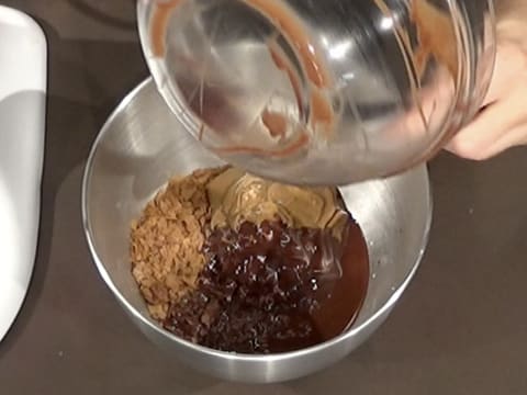 Le mélange de chocolat noir et de beurre de cacao fondus est versé dans la cuve du batteur, sur le crumble, le pailleté feuilletine et le praliné noisette
