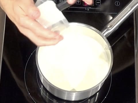 Vue de dessus de la casserole qui contient la crème liquide et le sirop de glucose, et dans laquelle on y ajoute le sucre inverti