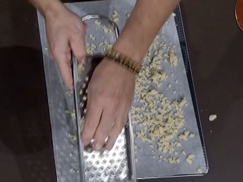 La pâte à crumble amande est écrasée sur la grille à Spätzel, et des morceaux de crumble tombent sur le papier sulfurisé