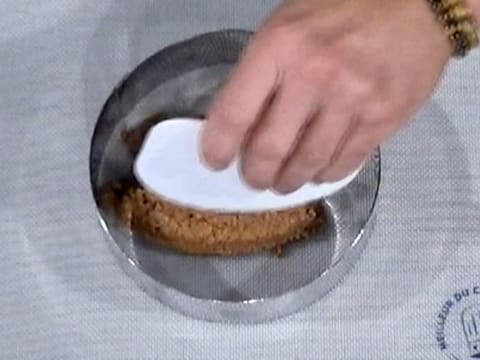 Un peu de croustillant est placé dans le cercle à mousse qui est posé sur un tapis de cuisson silicone