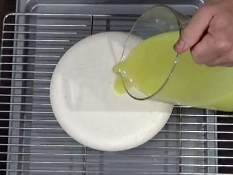 Le glaçage vert est versé sur l'entremets qui est sur une grille, elle-même placée sur une plaque creuse