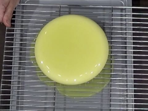 La grille sur laquelle est posé l'entremets nappé de glaçage vert, est tapotée sur la plaque creuse