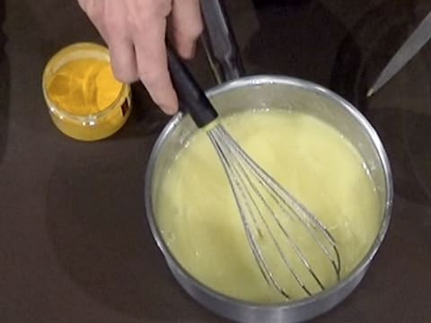 Mélange de la préparation crémeuse et du colorant jaune dans la casserole, à l'aide du fouet