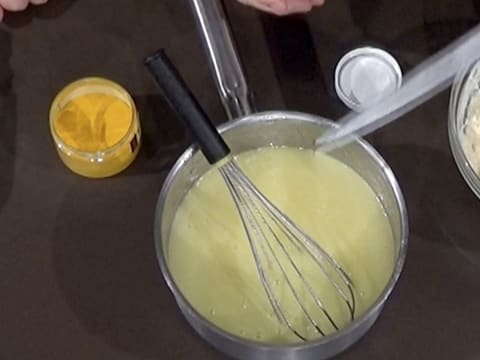 Ajout d'une pointe de colorant vert dans la casserole sur la préparation crémeuse
